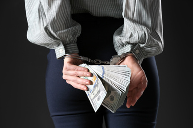 Photo of Woman in handcuffs holding bribe money on black background, closeup