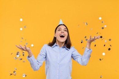 Photo of Happy young woman in party hat near flying confetti on yellow background