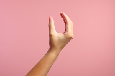 Photo of Woman holding something in fingers on pink background, closeup