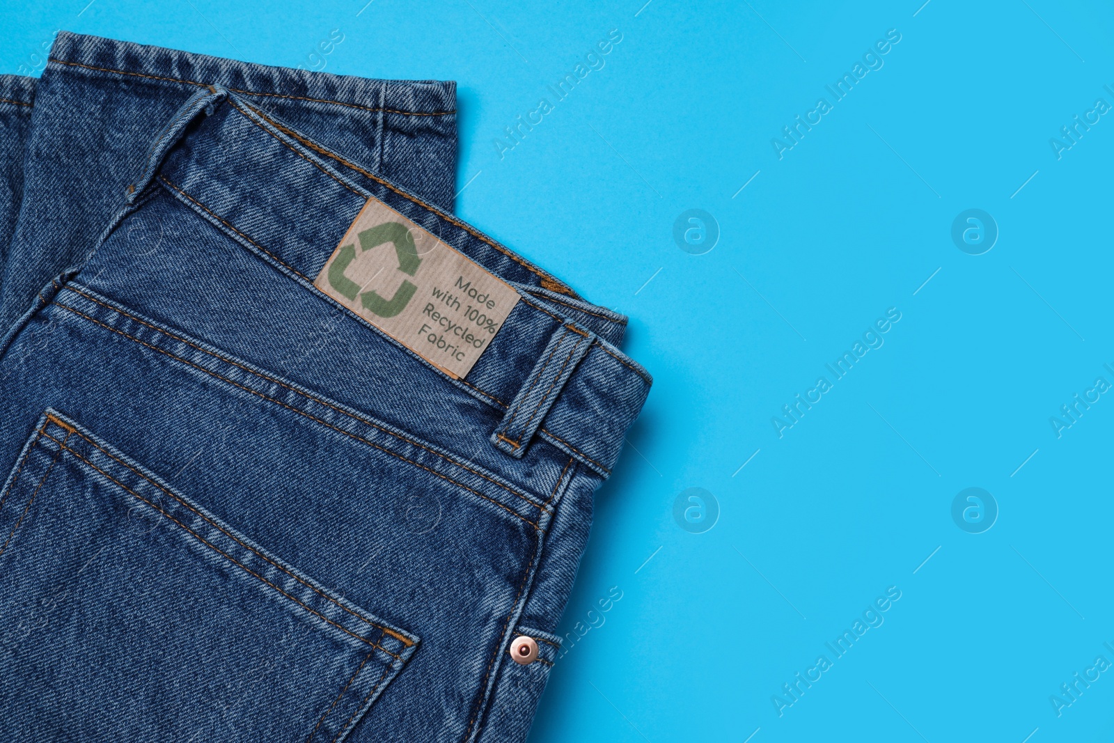 Photo of Jeans with recycling label on light blue background, top view. Space for text