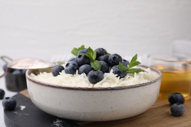 Photo of Bowl of delicious rice porridge with blueberries and mint served on table, space for text