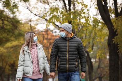 Photo of Couple in medical masks walking outdoors on autumn day. Protective measures during coronavirus quarantine