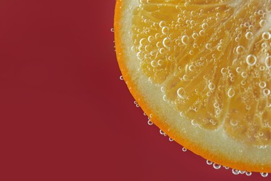 Photo of Fresh orange slice in sparkling water on red background, closeup. Space for text