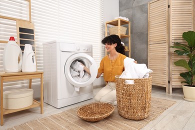 Happy woman putting laundry into washing machine indoors