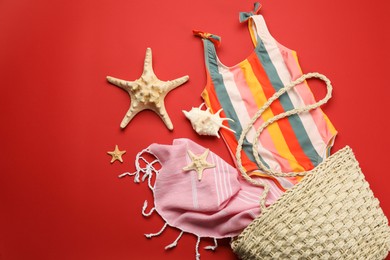 Photo of Stylish bag with beach accessories on red background, flat lay