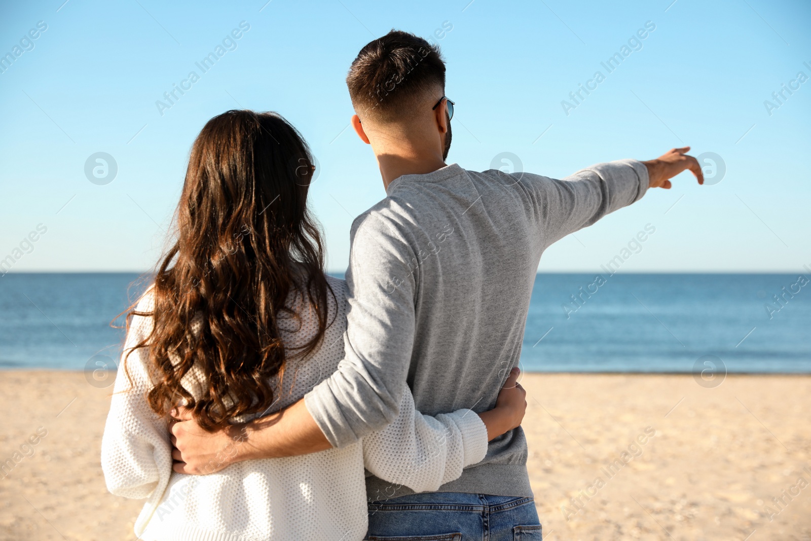 Photo of Young couple on beach near sea, back view. Honeymoon trip