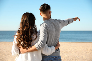 Photo of Young couple on beach near sea, back view. Honeymoon trip