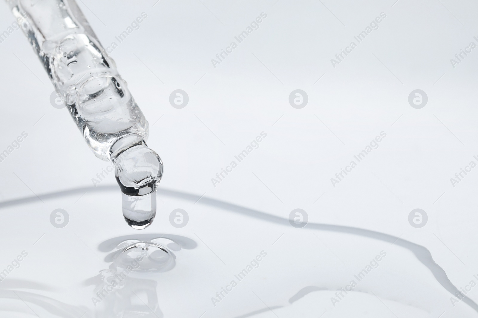 Photo of Dripping face serum from pipette on white background, closeup. Space for text