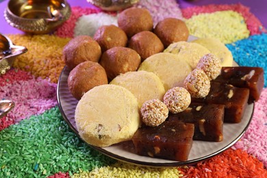 Diwali celebration. Tasty Indian sweets, colorful rangoli and diya lamps on table, closeup