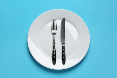 Photo of Clean plate with shiny silver cutlery on light blue background, top view