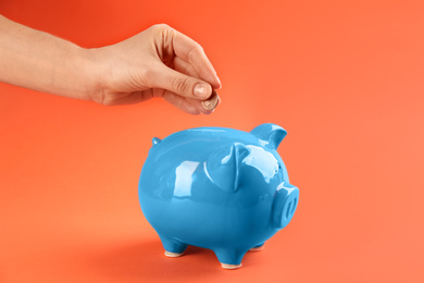 Woman putting coin into piggy bank on orange background, closeup