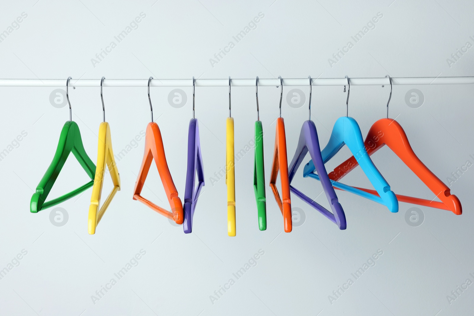 Photo of Bright clothes hangers on metal rail against light background