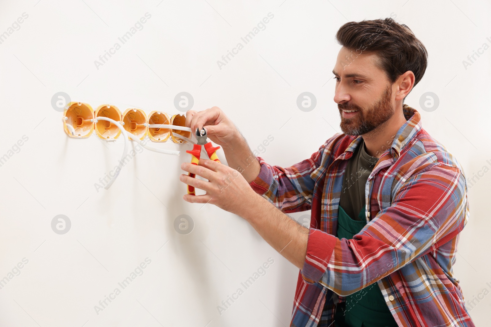 Photo of Professional electrician with pliers fixing wires indoors