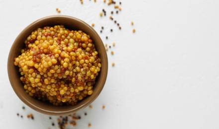 Photo of Fresh whole grain mustard in bowl and dry seeds on white table, flat lay. Space for text