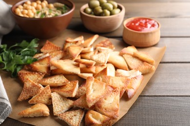 Delicious pita chips with hummus, olives and sauce on wooden table, closeup