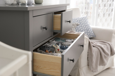 Modern open chest of drawers with baby clothes and accessories in room, closeup