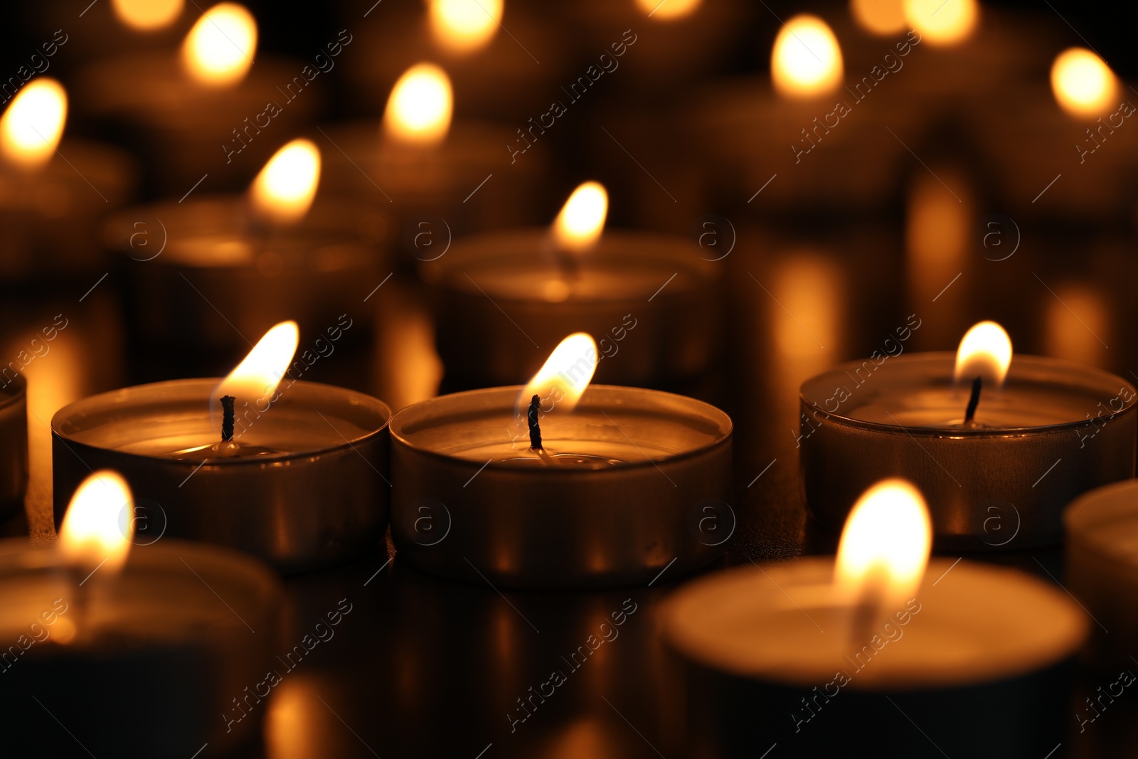 Photo of Burning tealight candles on dark surface, closeup