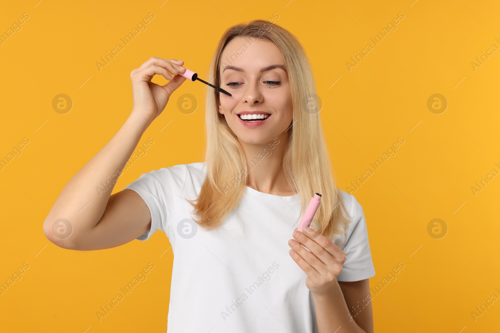 Photo of Beautiful woman applying mascara on orange background