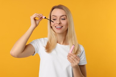 Photo of Beautiful woman applying mascara on orange background