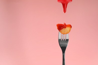 Photo of Pouring ketchup onto tasty baked potato on fork against pink background, closeup. Space for text