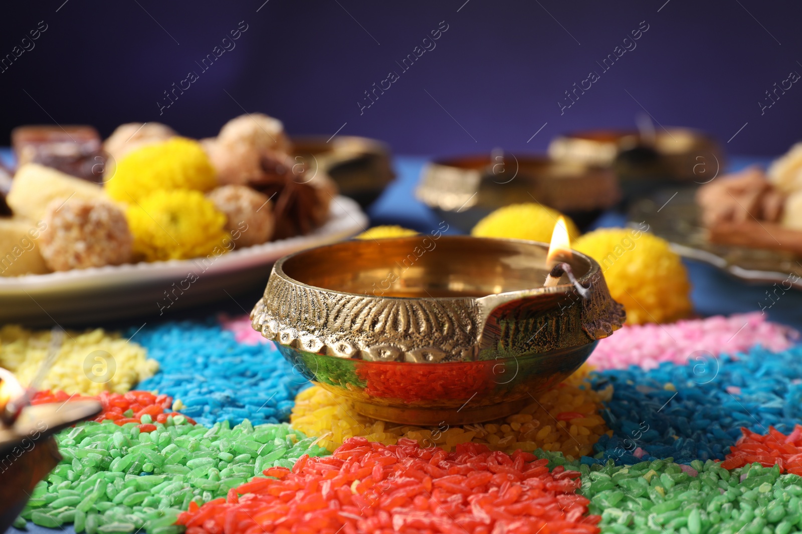 Photo of Diwali celebration. Diya lamps and colorful rangoli on table against violet background, closeup