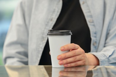 Woman holding takeaway paper cup at table, closeup. Coffee to go