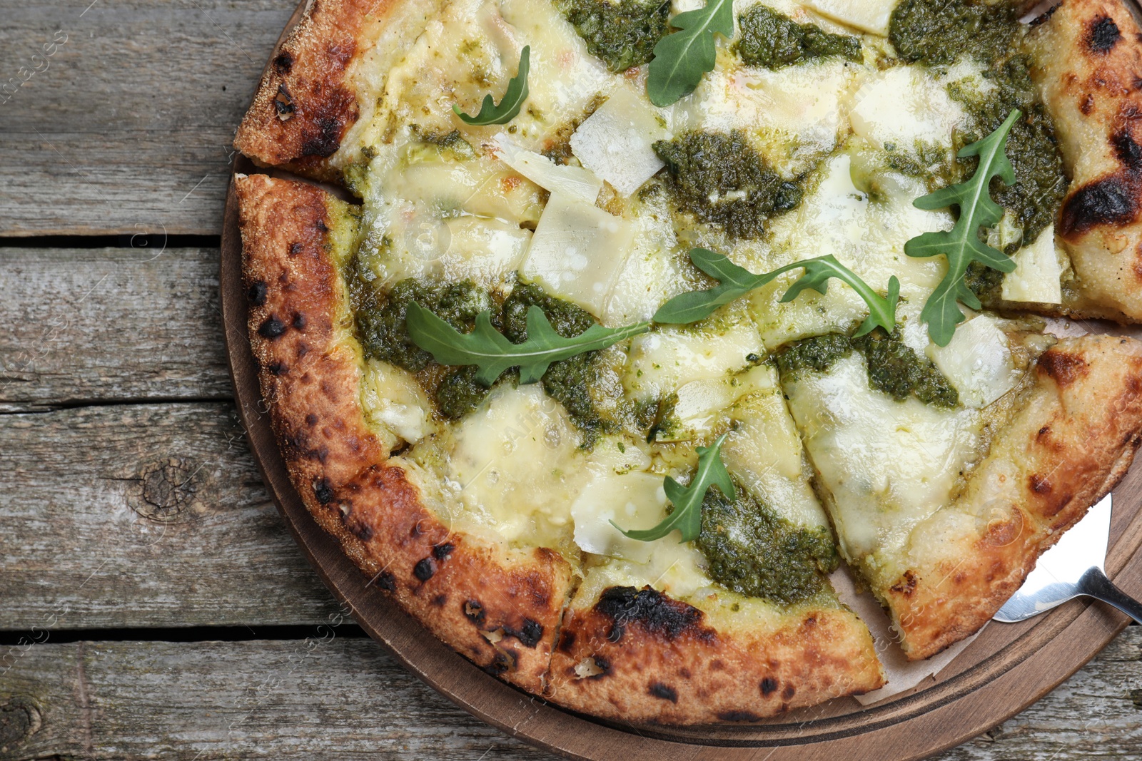 Photo of Delicious pizza with pesto, cheese and arugula on wooden table, top view