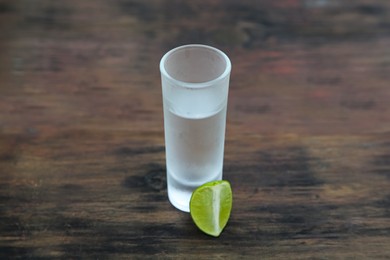 Photo of Mexican tequila shot with lime slice on wooden table. Drink made from agave