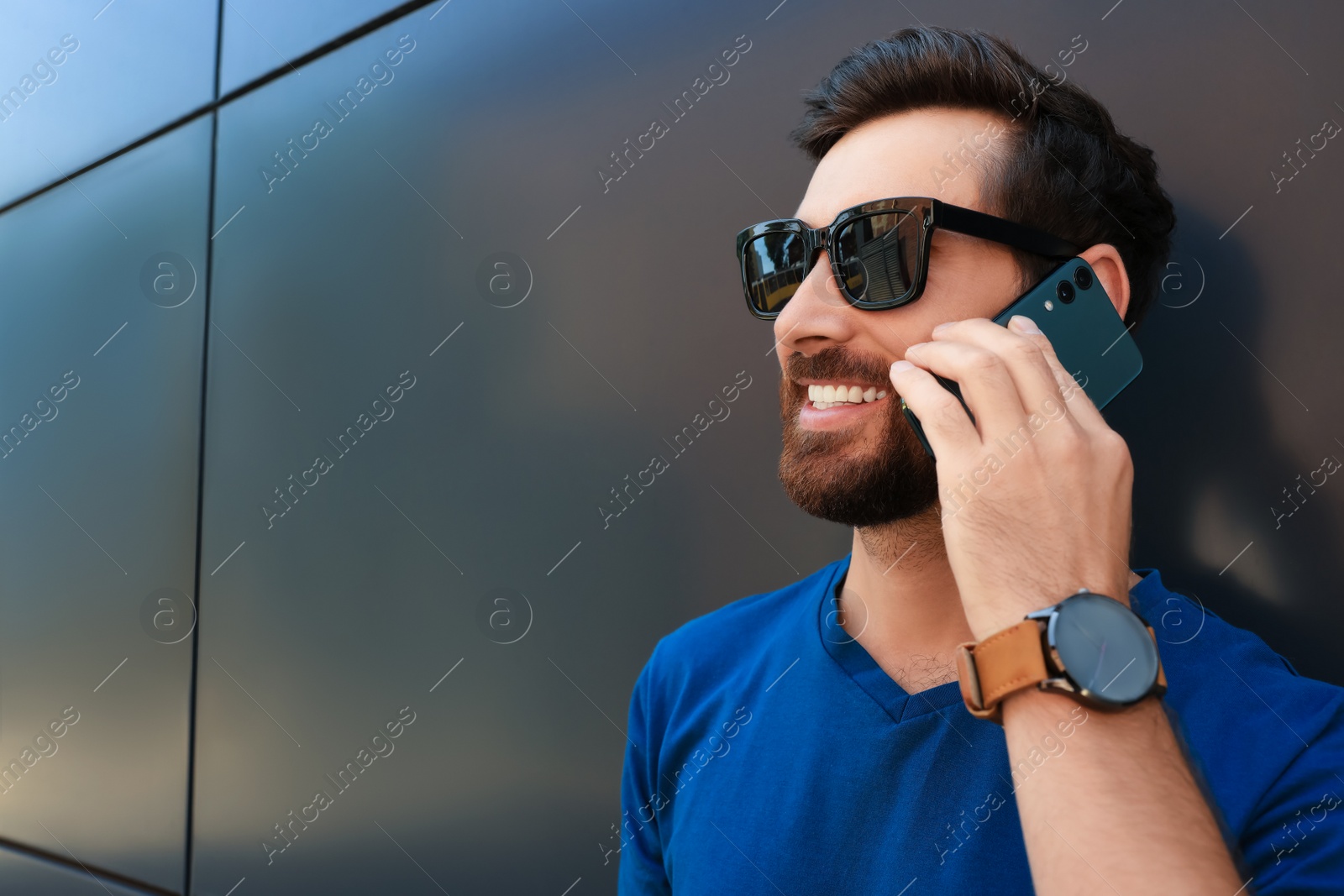 Photo of Happy man talking on phone near grey wall. Space for text