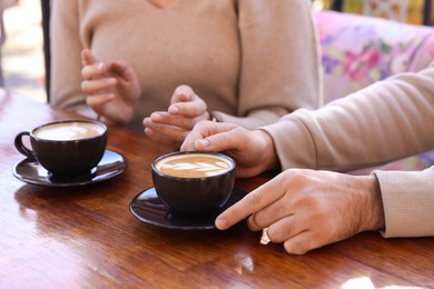 Couple with cups of aromatic coffee at wooden table, closeup