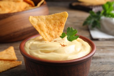Delicious cheese sauce with nacho and parsley on table, closeup