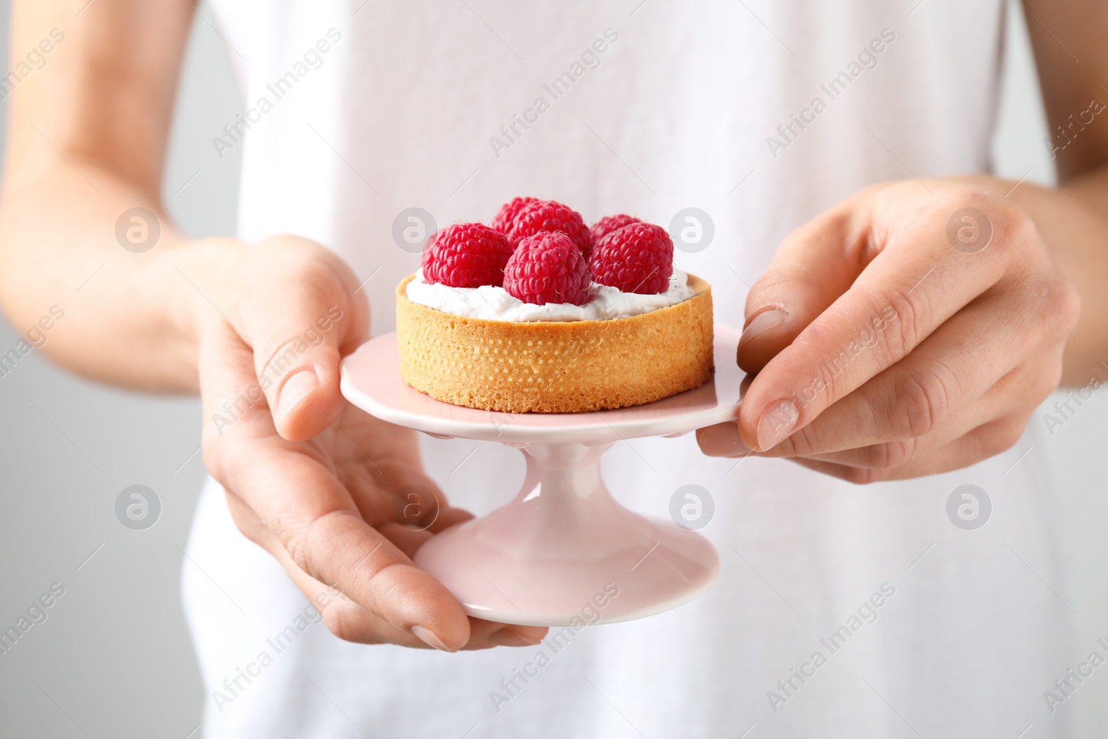 Photo of Woman holding cake stand with raspberry tart, closeup. Delicious pastries