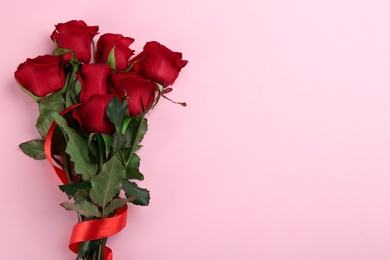 Photo of Beautiful red roses with ribbon and space for text on pink background, top view. Valentine's Day celebration