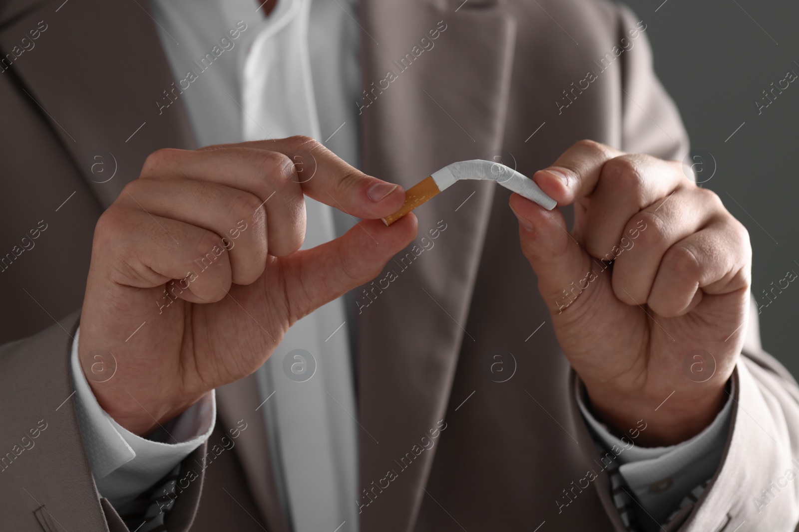 Photo of Stop smoking concept. Man breaking cigarette on gray background, closeup