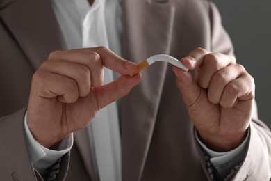 Stop smoking concept. Man breaking cigarette on gray background, closeup