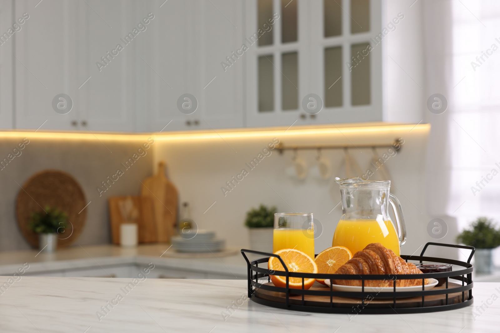 Photo of Breakfast served in kitchen. Tray with fresh croissant, jam and orange juice on white table, space for text