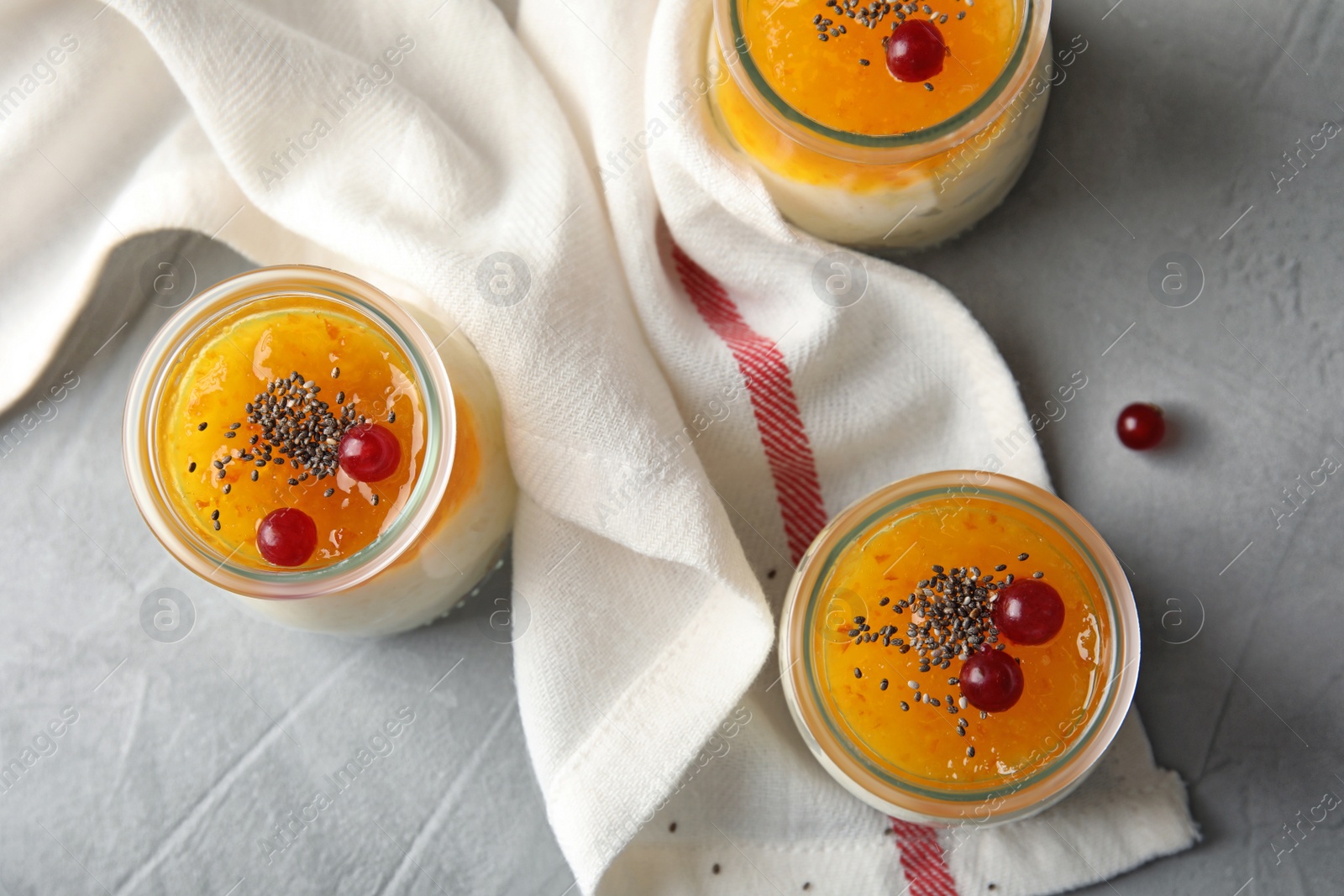 Photo of Creamy rice pudding with red currant and jam in jars on grey table, top view