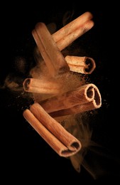 Image of Aromatic cinnamon sticks and powder flying on black background