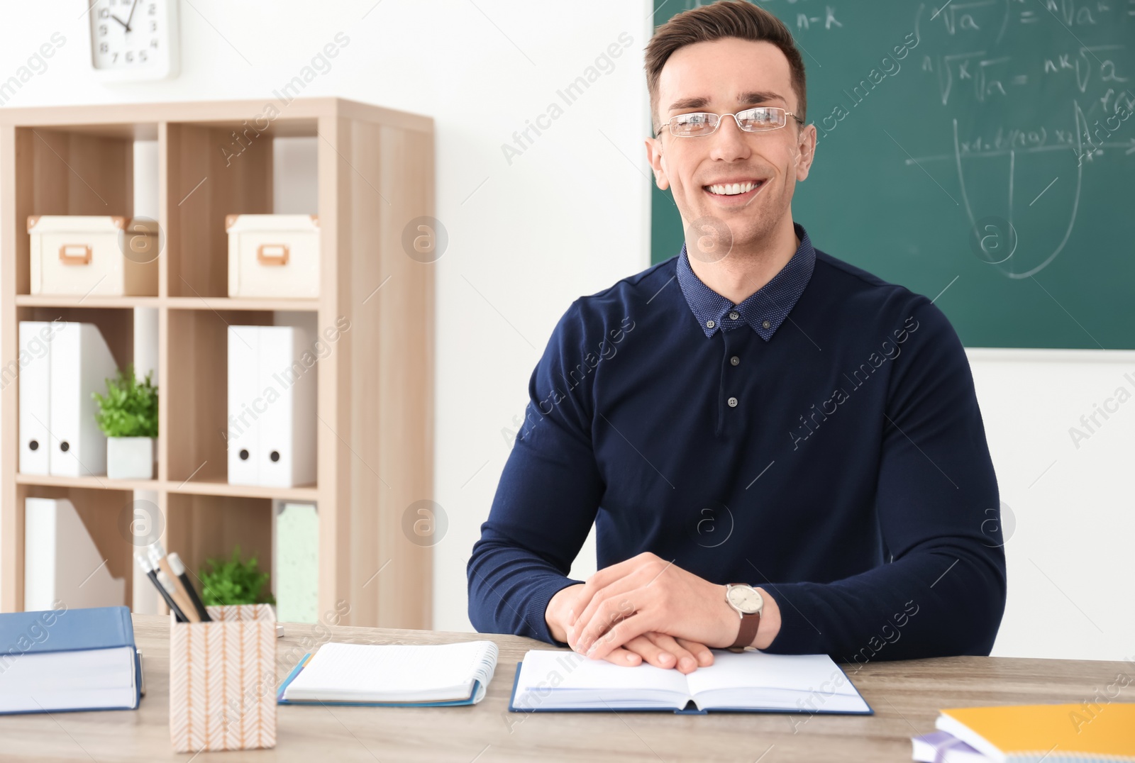 Photo of Young male teacher with book sitting at table in classroom