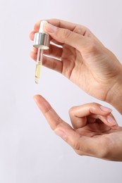 Photo of Woman applying cosmetic serum onto her finger on white background, closeup