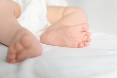 Photo of Little baby with cute feet on bed sheet, closeup