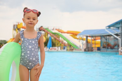 Photo of Cute little girl with inflatable ring near pool in water park, space for text