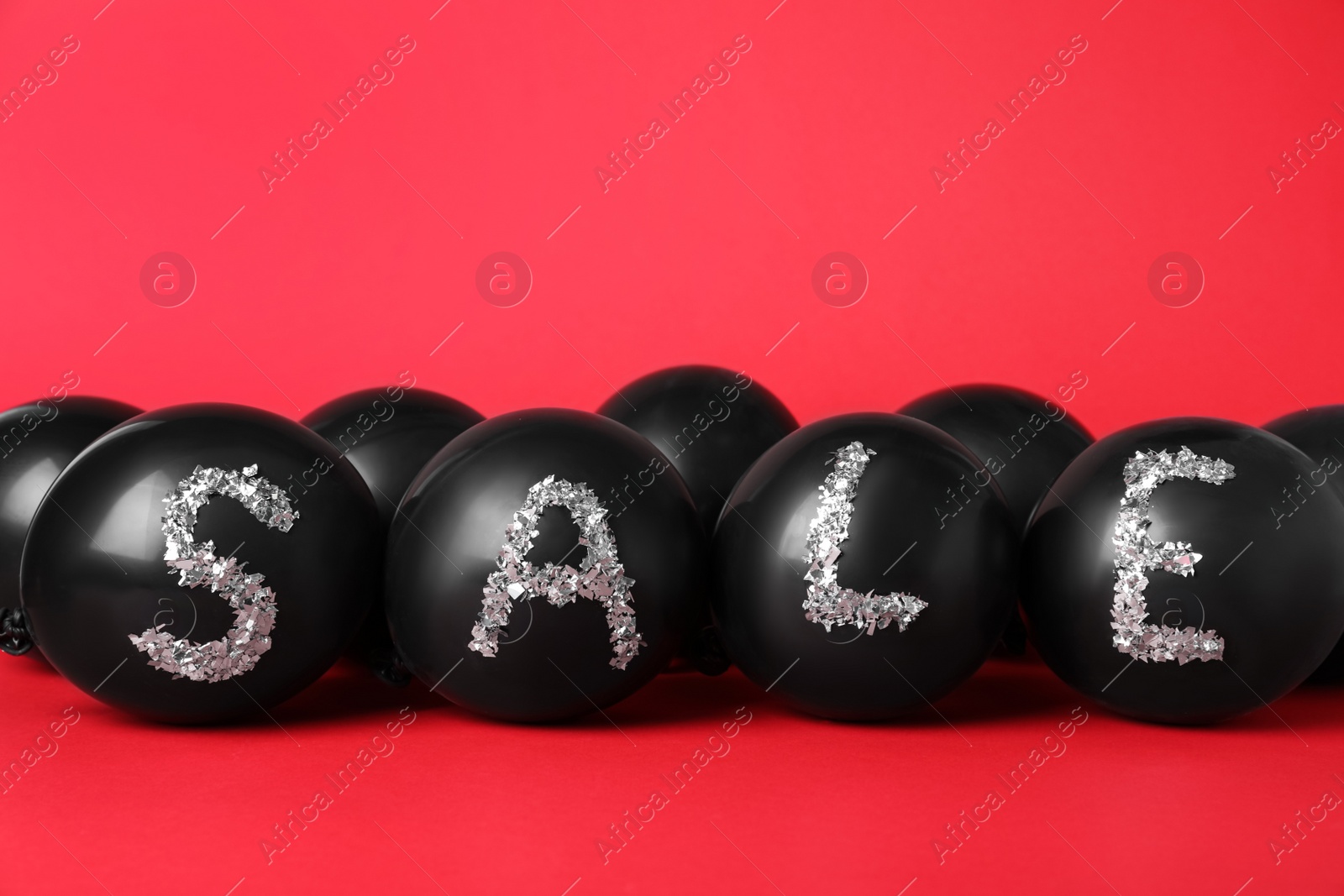Photo of Word Sale made of balloons and metallic confetti on red background. Black Friday
