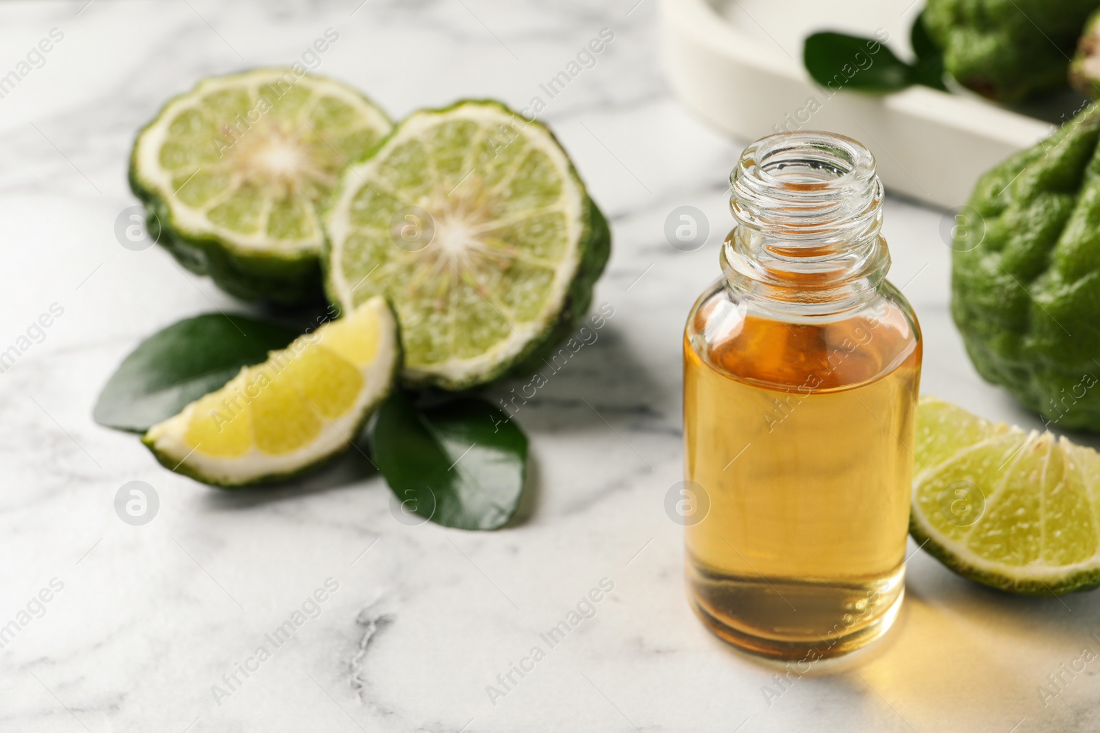 Photo of Bottle of essential oil and fresh bergamot fruits on white marble table. Space for text