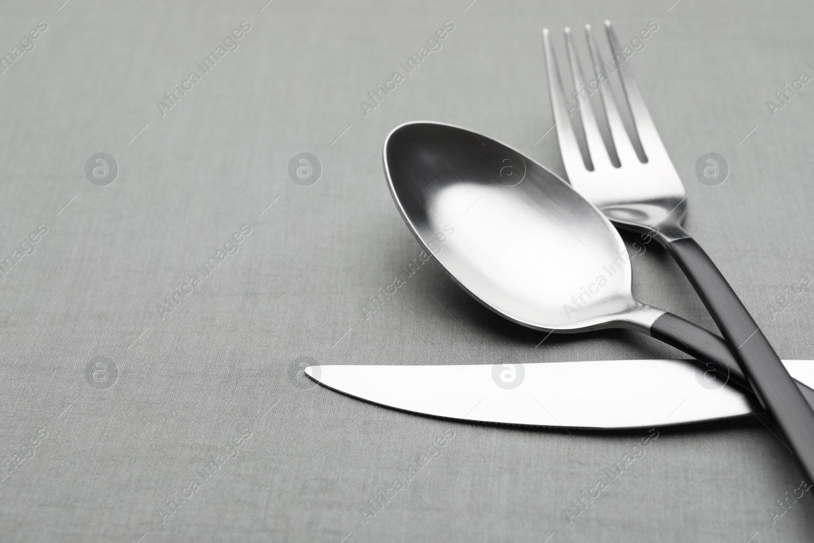 Photo of Set of shiny silver cutlery on grey table, closeup. Space for text