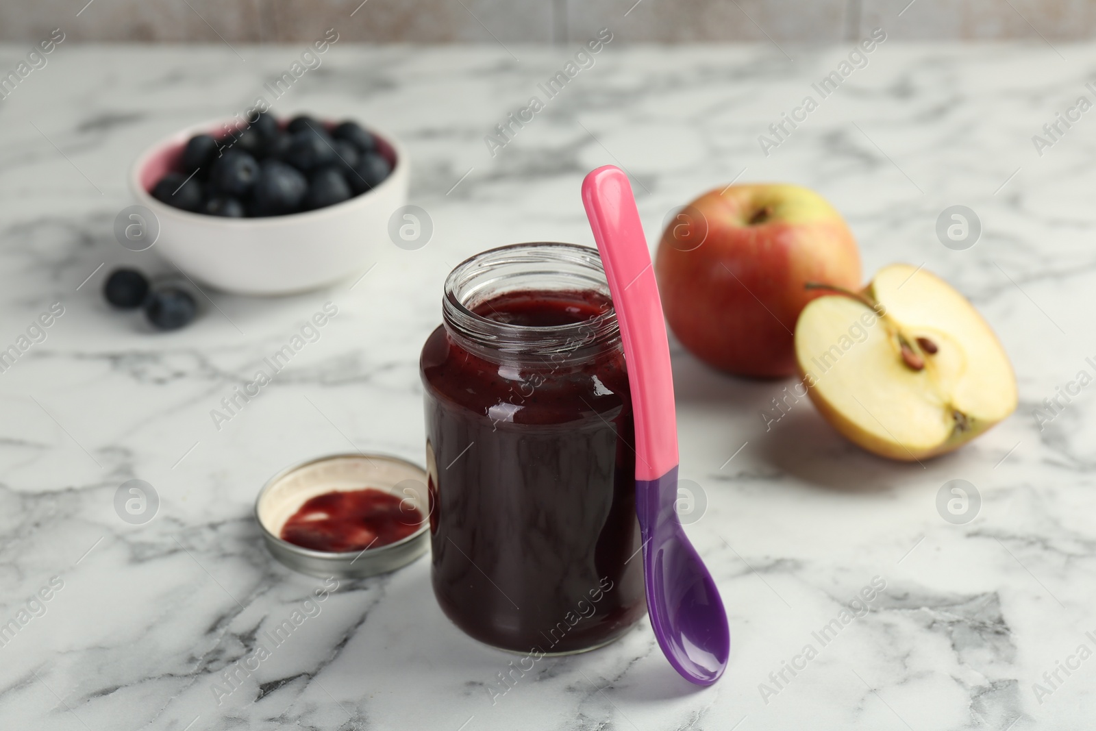 Photo of Tasty baby food in jar and spoon on white marble table