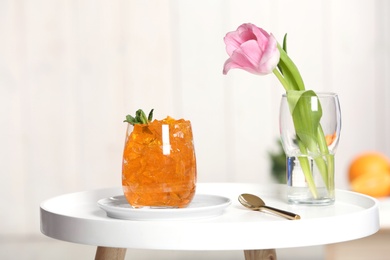 Photo of Glass of jelly and flower on table against blurred background