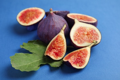 Photo of Delicious ripe figs with green leaf on blue background, closeup