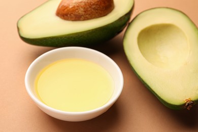 Cooking oil in bowl and fresh avocados on beige background, closeup