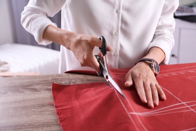 Photo of Tailor cutting fabric at table in atelier, closeup